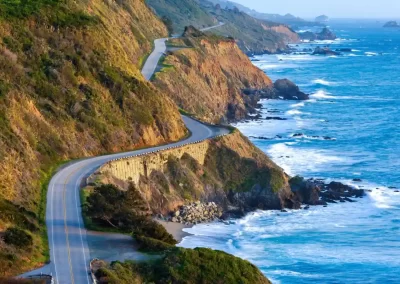 Pacific Coast Highway winding along rugged cliffs beside the blue Pacific Ocean in California.