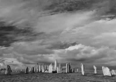 Wide black-and-white view of the Callanish Standing Stones beneath a dramatic cloud-filled sky on the Isle of Lewis.