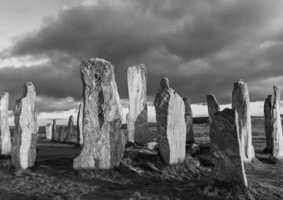 Black-and-white view of the ancient Callanish Standing Stones beneath dramatic clouds on the Isle of Lewis.