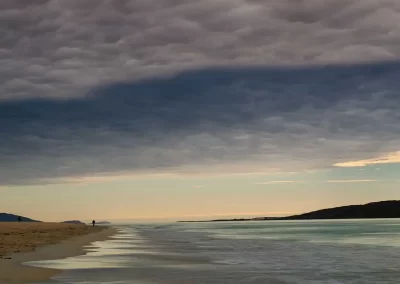 Lone figure walking along Luskentyre Beach beneath dramatic evening clouds in South Harris, Scotland.