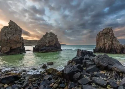 Rocky sea stacks rising from turquoise water beneath a dramatic evening sky at Garry Beach, Isle of Lewis.