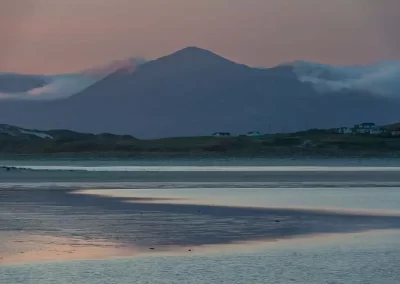 Tidal sands and shallow water beneath a cloud-wrapped mountain at dusk in Lewis and Harris, Scotland.