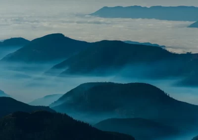 Layered forested mountains rising through low cloud and mist near Tofino on Vancouver Island, photographed by Garth Lenz.