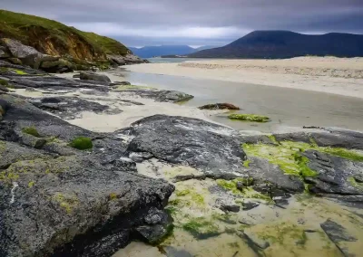 Seaweed-covered rocks, white sand and distant mountains at Horgabost Beach on the Isle of Harris, Scotland.