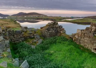 Ruined stone croft overlooking coastal lochs and a remote settlement in South Harris, Scotland.