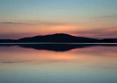 Mountain silhouette reflected in calm water beneath a colourful sunset in South Harris, Scotland.