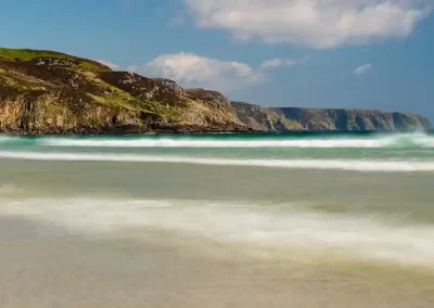 Turquoise Atlantic waves and sunlit cliffs at Garry Beach on the Isle of Lewis, Scotland.