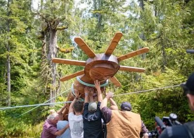 Indigenous community members raising a carved wooden totem pole among the coastal rainforest trees of British Columbia. Photo courtesy of IISAAK OLAM Foundation.
