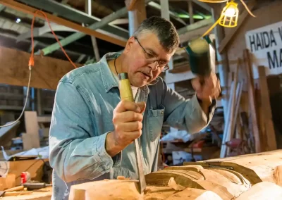 Woodcarver using a mallet and chisel to create a traditional carving near Tofino, British Columbia, photographed by Garth Lenz.