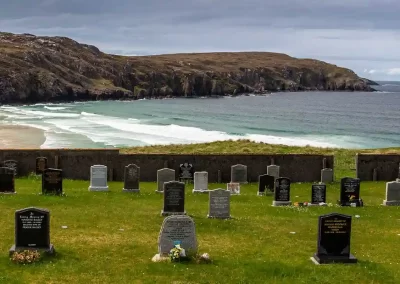 Coastal cemetery overlooking a sandy bay, turquoise waves and rugged cliffs on the Isle of Lewis, Scotland.