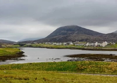 Coastal village beneath a mist-covered mountain beside a sea loch in South Harris, Scotland.